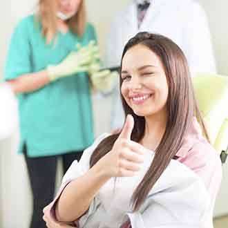 Smiling patient giving thumbs up while sitting in treatment chair